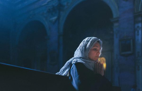 Female with a head covering sitting in a place of worship with hands together in prayer