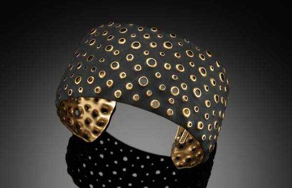 Jewelry. Black metal bracelet with holes punched through showing the gold under color.